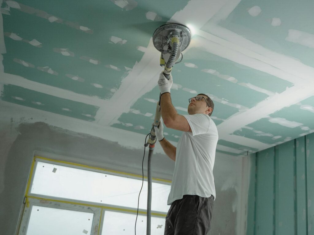 pexels-photo-6474343-6474343-1 A professional worker sanding the ceiling during a home renovation project. Indoor construction setting.